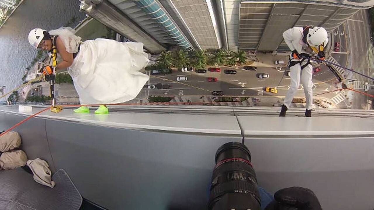 Bride and groom rappel down hotel building in wedding attire