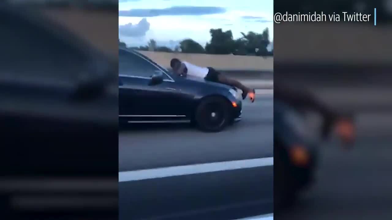 Man clings to car's  hood as it drives on I-95 in Miami